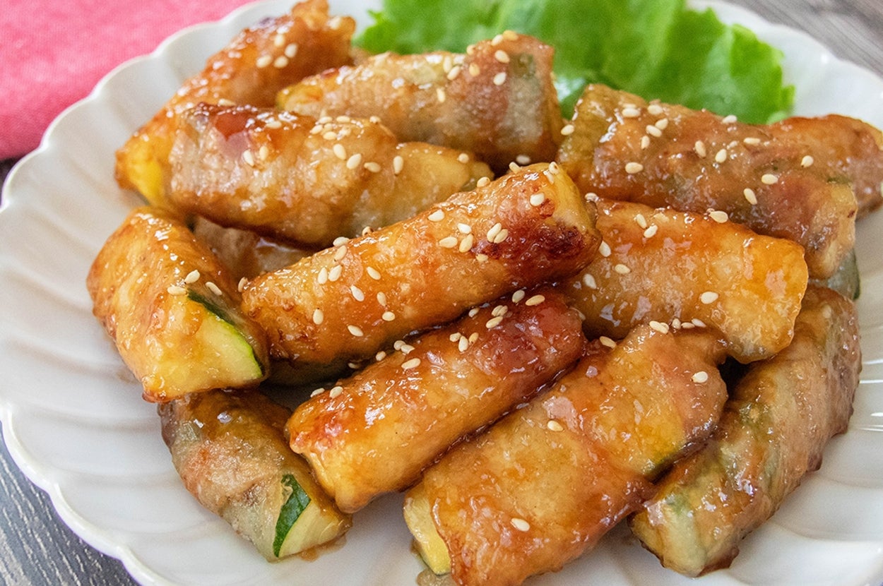 お皿に盛られた肉巻きズッキーニ。白いりごまがトッピングされ、美味しそうに焼き上がっている。バックにレタスが添えられている。