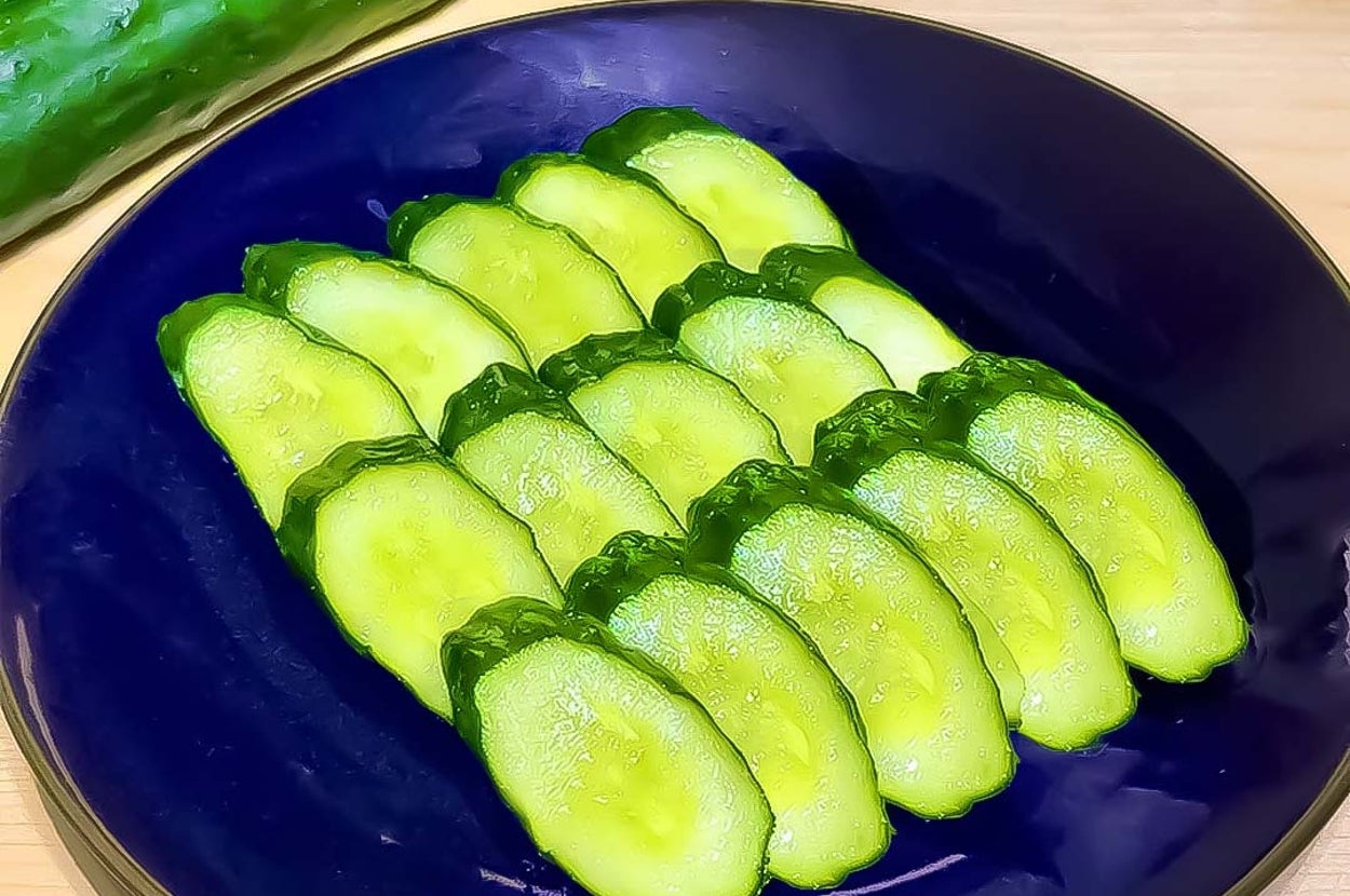 お皿に盛られた薄くスライスされたキュウリが整然と並んでいる。バッグラウンドに丸ごとのキュウリ。