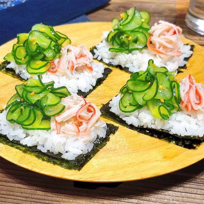 寿司風の料理が木の皿に盛られており、キュウリとカニの具材がそれぞれ乗っている。