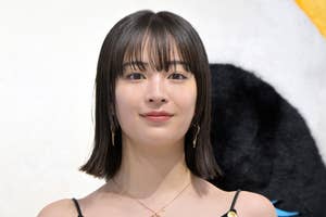 セレブが黒いボタンの付いた白いドレスを着て、ルイ・ヴィトンのバッグを持ちながらイベントでポーズを取っている。