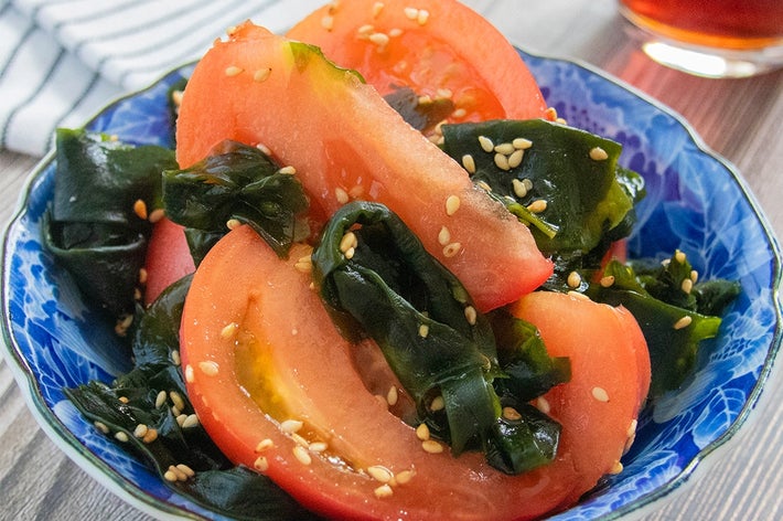 トマトとわかめのサラダが青い器に盛られています。背景に飲み物があります。