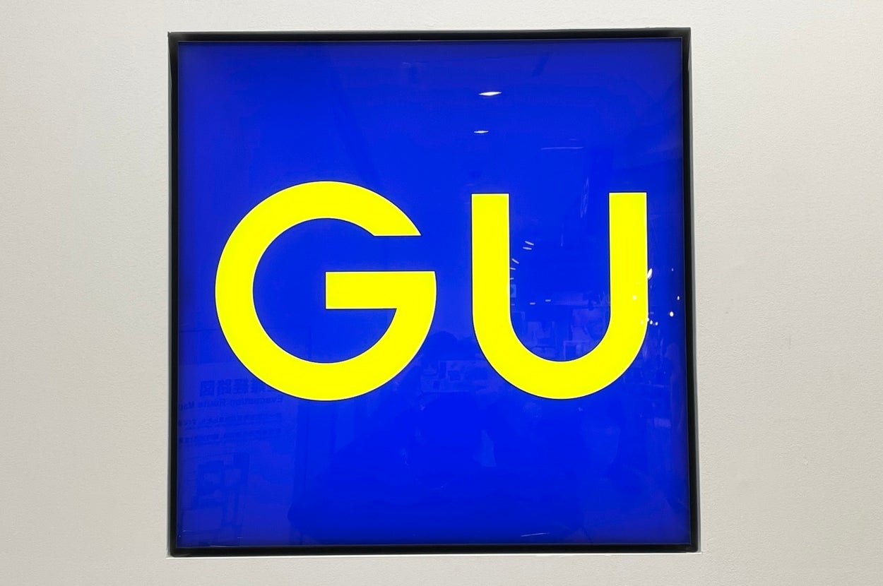 The image shows a sign with the letters "GU" in a bold, modern font