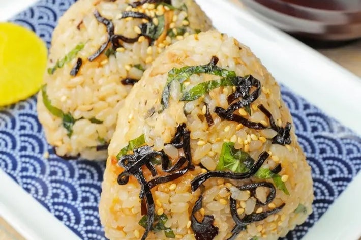 お皿にのった2つの塩昆布おにぎり。後ろに味噌汁と漬物が添えられている。