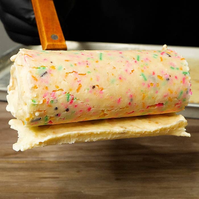 アイスクリームのロールがスプーンで持ち上げられている様子。カラフルなスプリンクルが混ざっている。