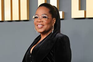 Oprah Winfrey smiling on a red carpet, with hoop earrings and round glasses