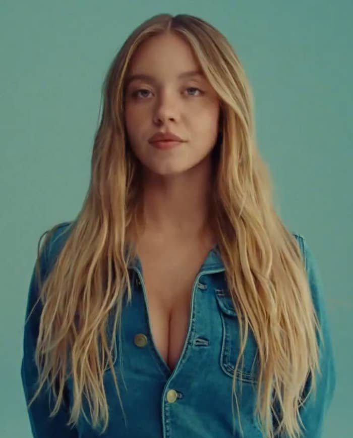 Person in a denim jacket with long hair facing forward against a plain backdrop