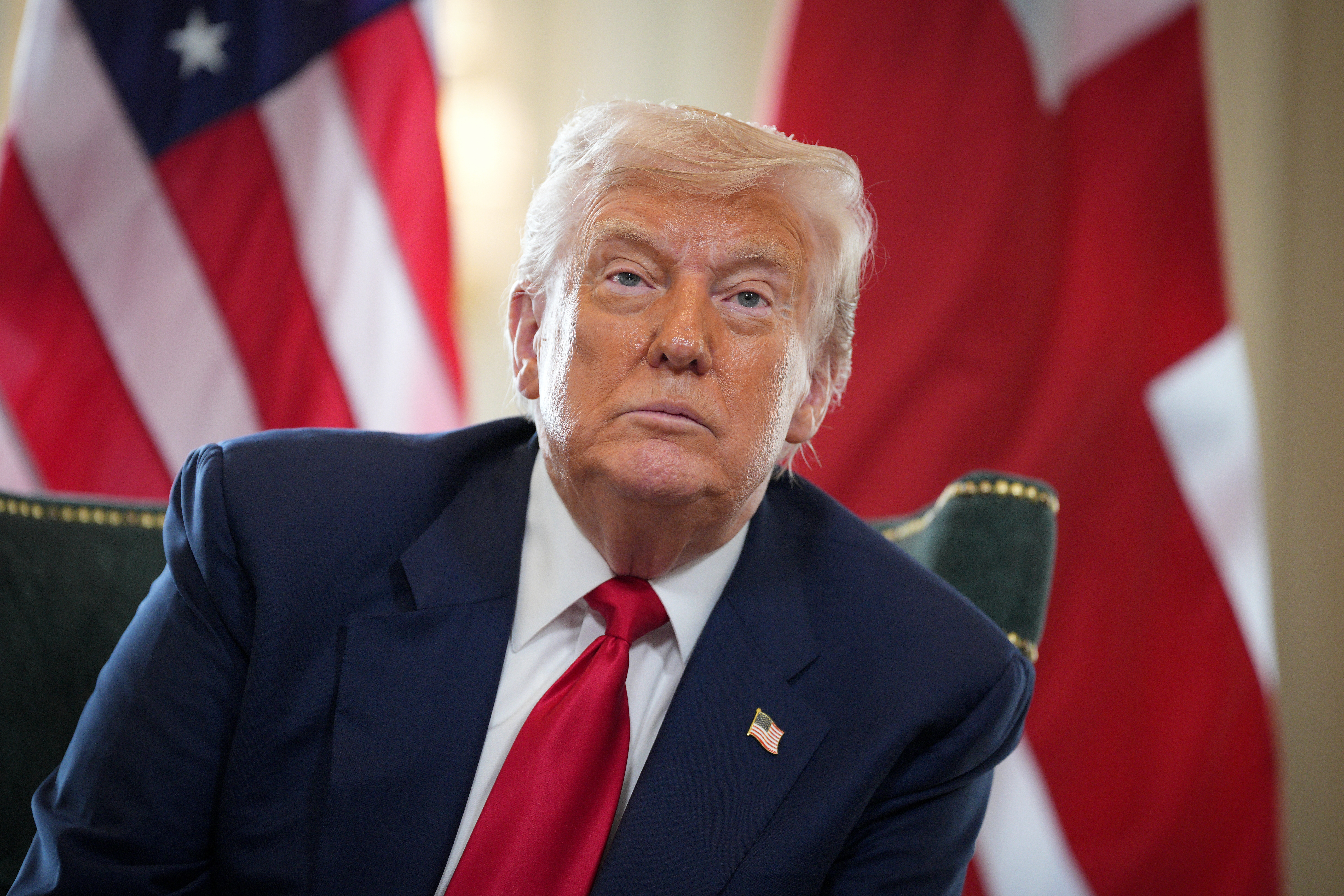 Man in a suit with a red tie sitting in front of American flags
