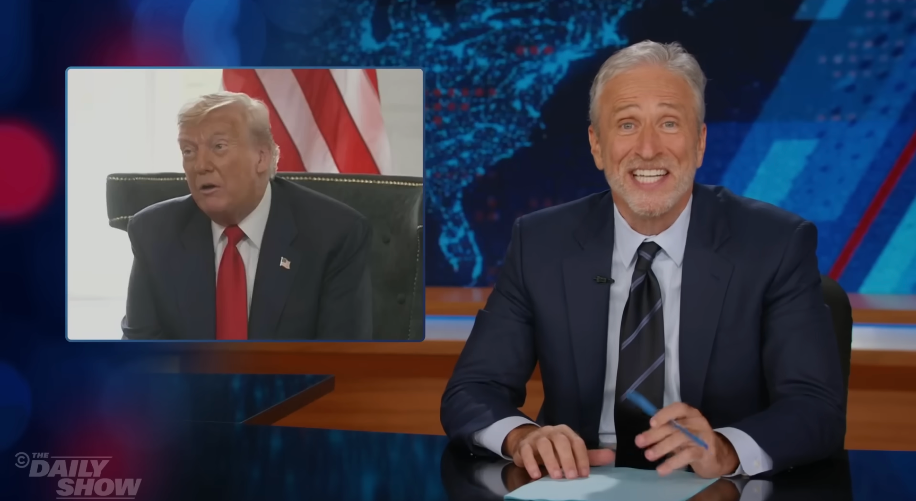 A TV host in a suit smiles at the camera in a studio. An image inset shows a man speaking, sitting beside an American flag