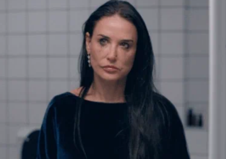 Person with long hair and earrings looks into the distance, wearing a velvet-like top in a tiled room