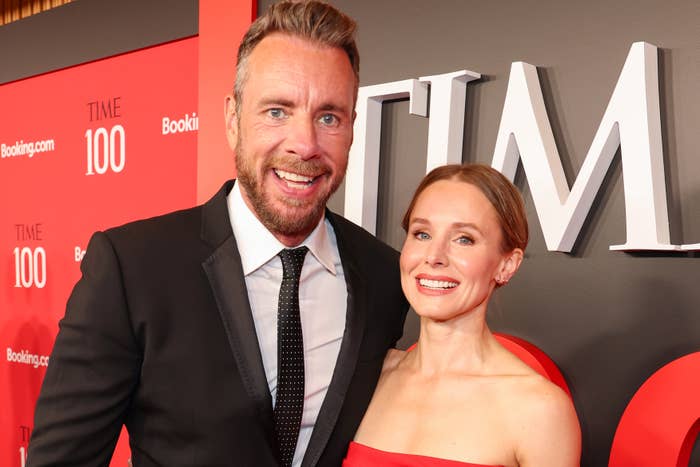 Dax Shepard and Kristen Bell posing together on a red carpet event. The woman wears a strapless dress, and the man is in a suit and tie