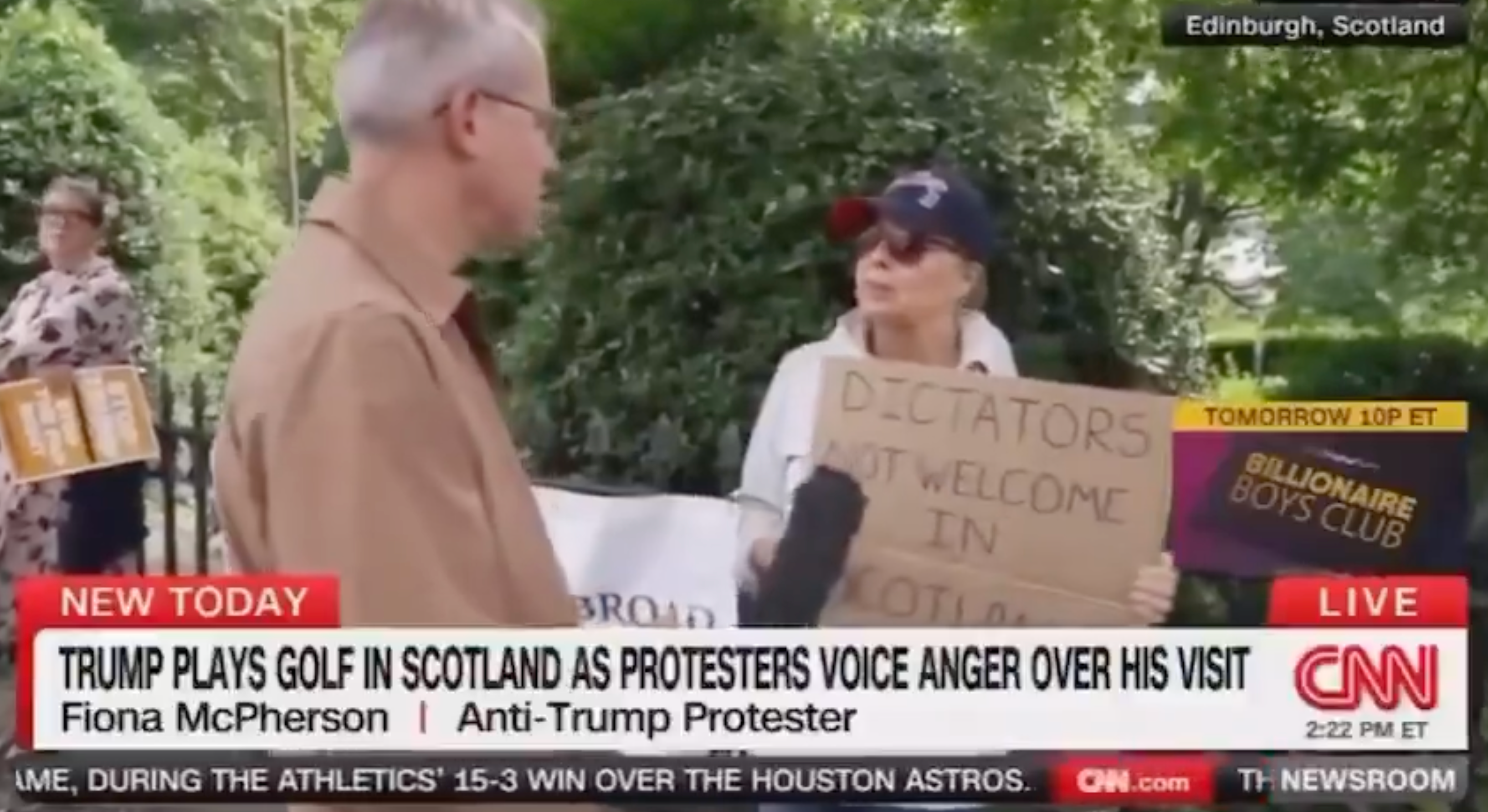Protester in sunglasses holds sign reading &quot;Dictators not welcome in Scotland&quot; during a CNN interview about Trump&#x27;s visit