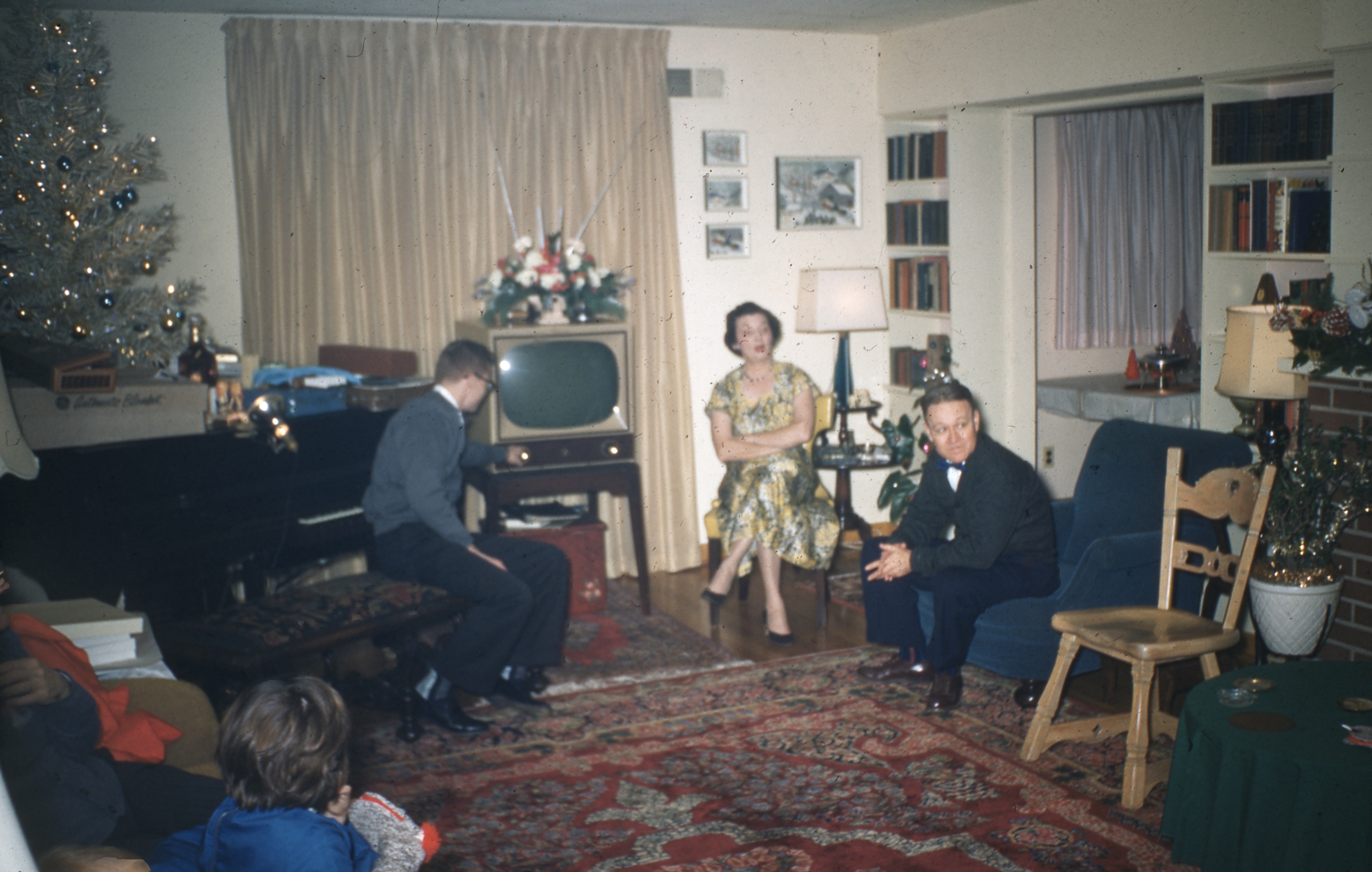 Family gathered in a living room with mid-century decor, decorated for the holidays, with a Christmas tree and a vintage TV set