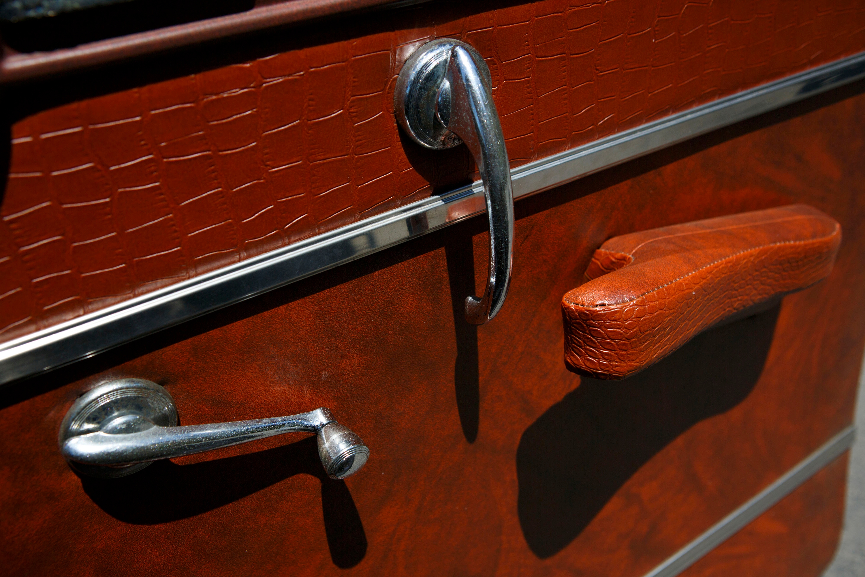 Close-up of a vintage car door with crank window handle and textured latch