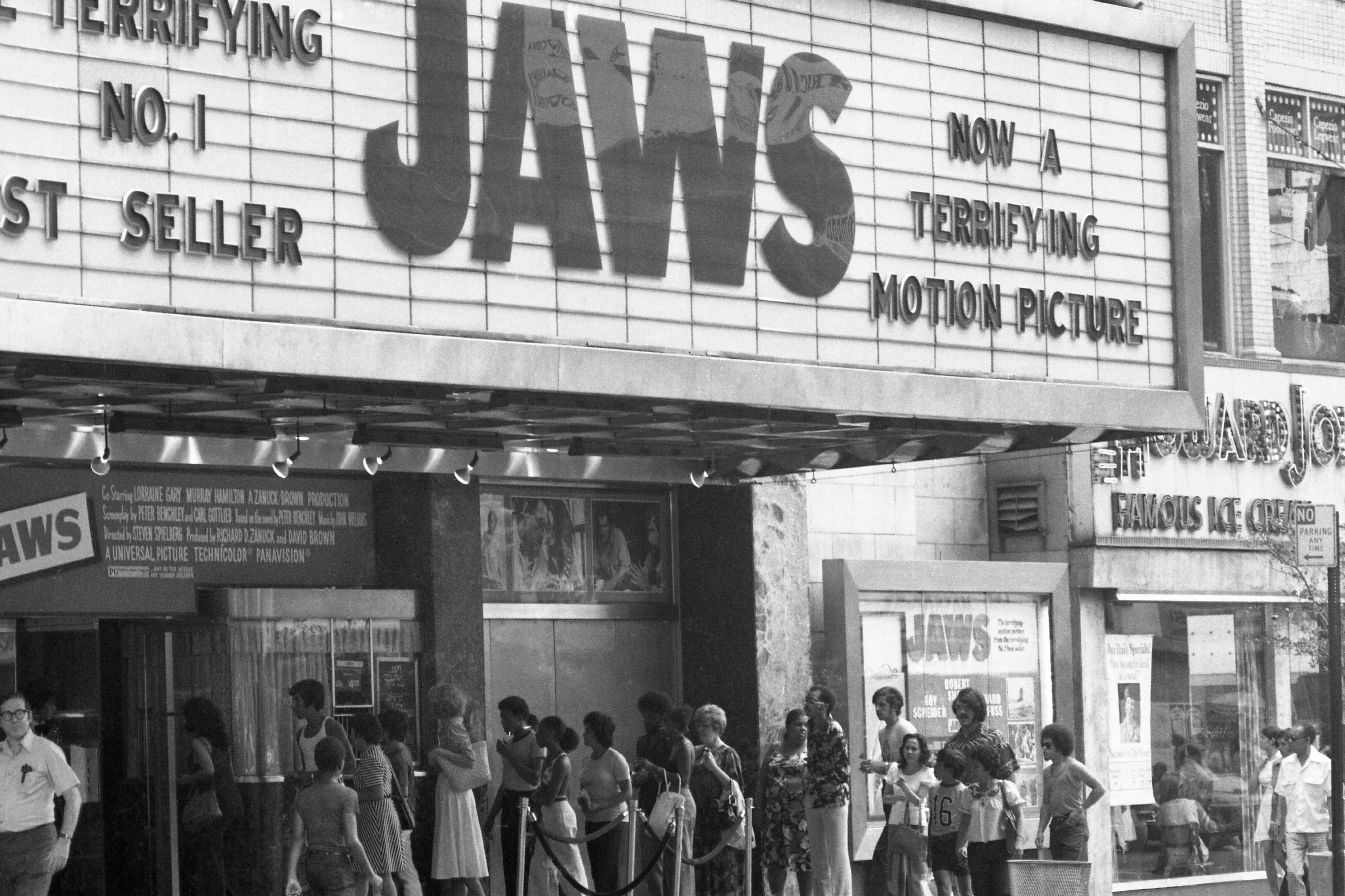 People lined up outside a theater showing "Jaws," with the marquee reading "NO. 1 BEST SELLER" and "NOW A TERRIFYING MOTION PICTURE."