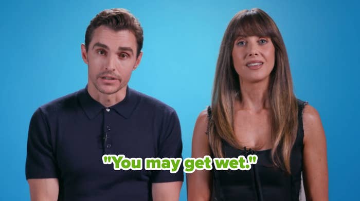Two people seated against a blue background. The person on the left wears a dark shirt, and the person on the right is in a sleeveless black top