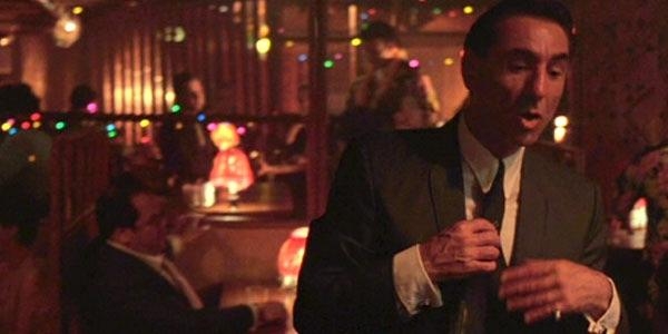 A man in a suit adjusts his tie in a dimly lit, bustling restaurant or bar scene