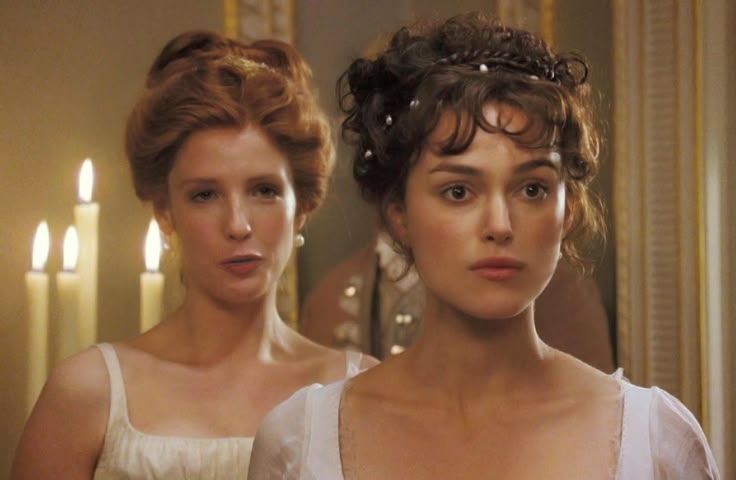 Escena de película de época con dos mujeres con peinados antiguos y vestidos elegantes, frente a candelabros