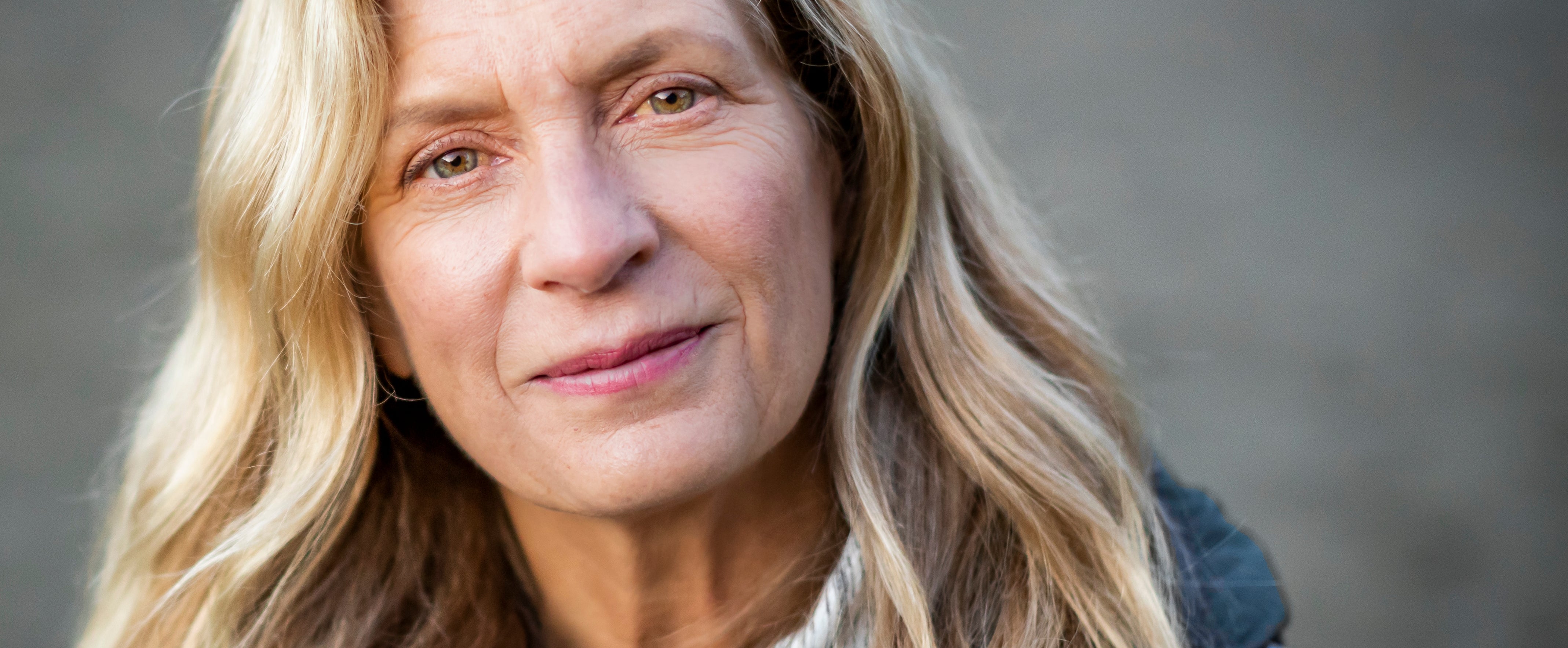 Person utendørs iført en lysjakke, smilende forsiktig