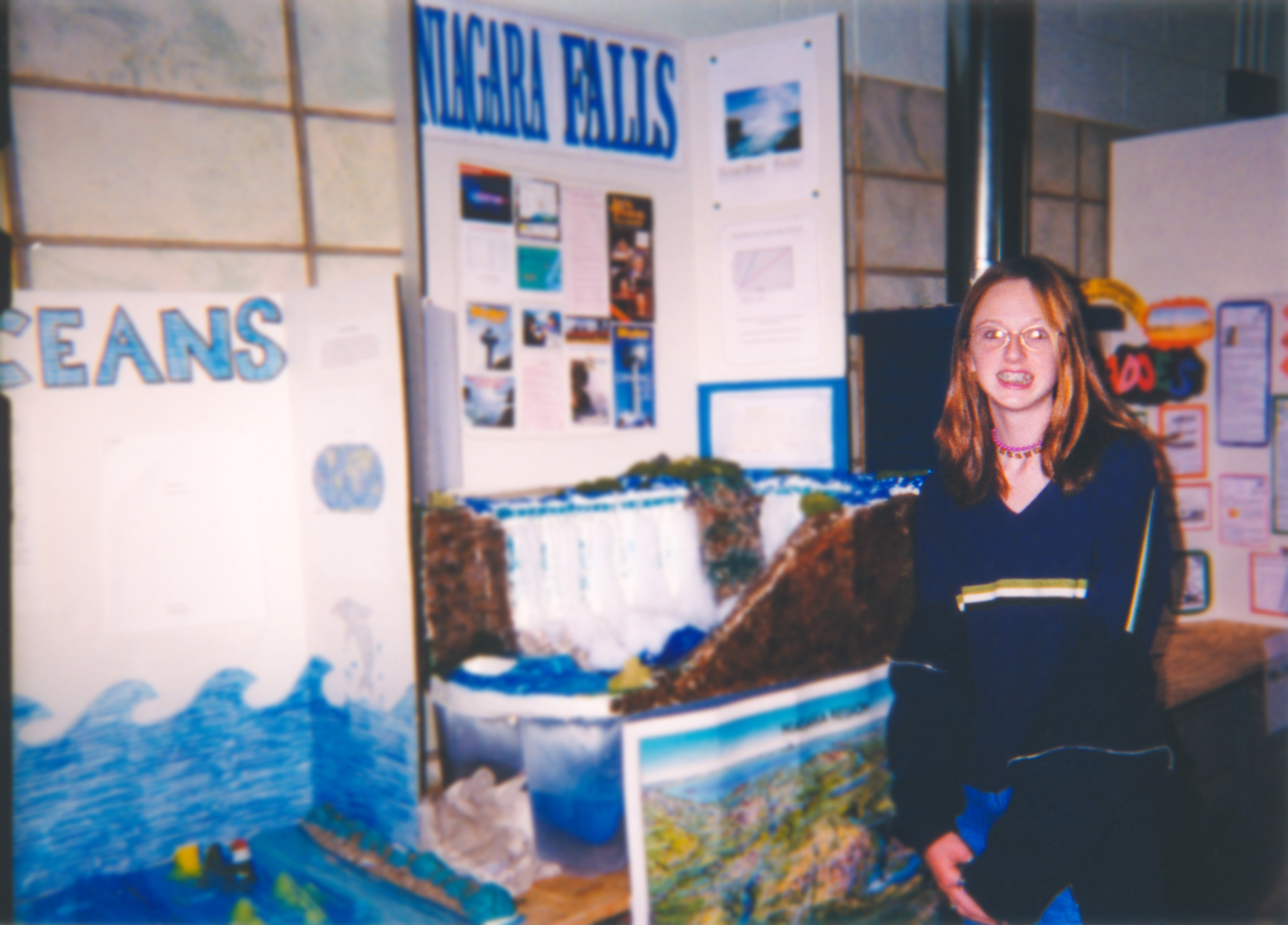 Person at a school science fair stands beside a Niagara Falls project display, featuring informational posters and a model waterfall
