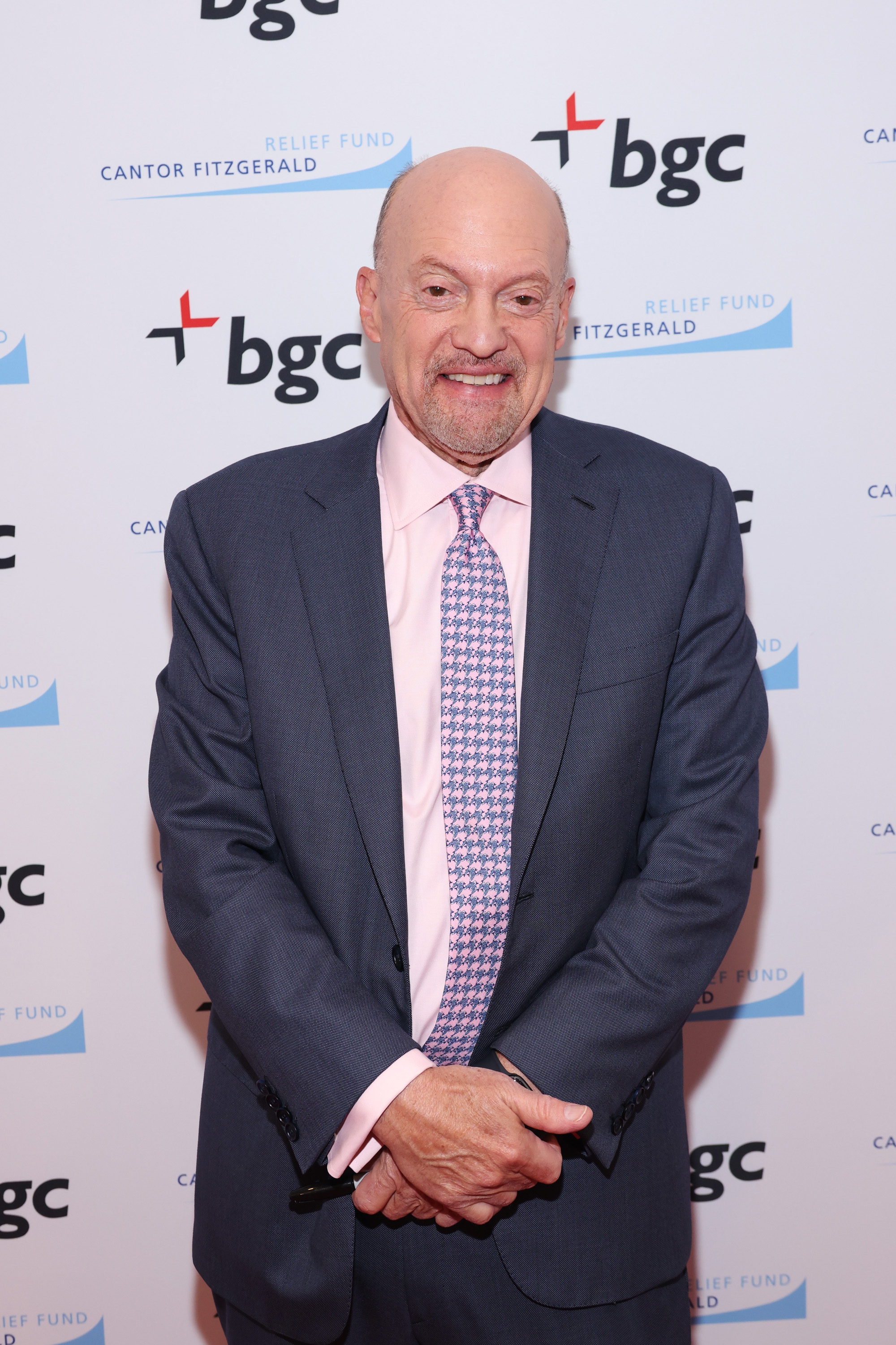 Person in a suit with a patterned tie, standing in front of a backdrop with logos
