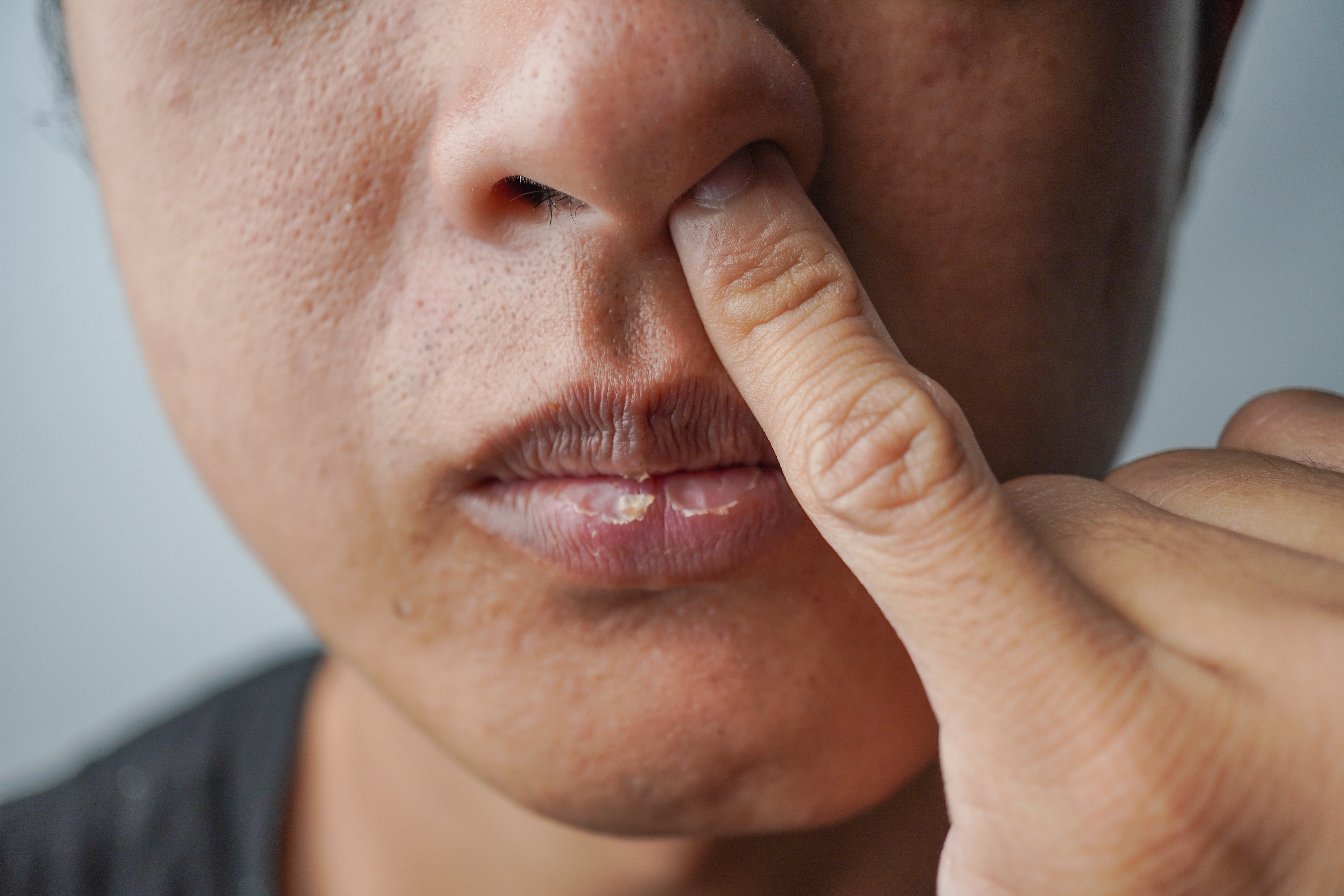 Person picking their nose with one finger visible. Close-up view of mouth and nose area