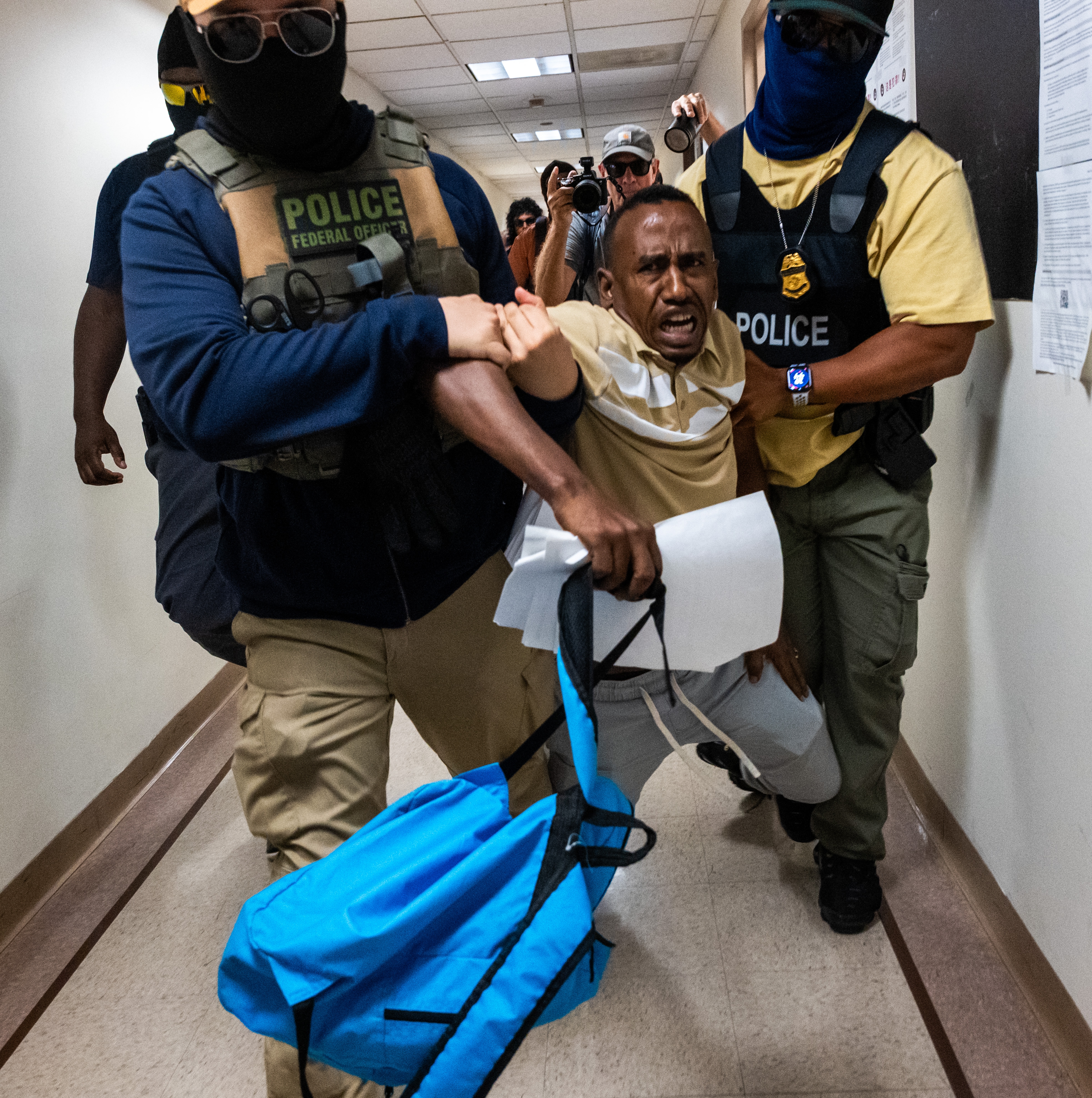 A man being escorted by police through a hallway, showing a tense and possibly urgent situation