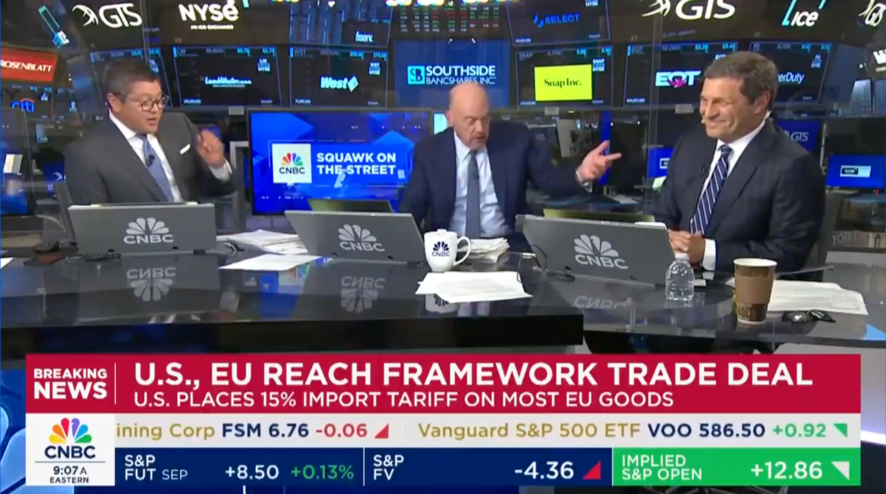Three news anchors discuss a U.S.-EU trade deal on a financial news set with stocks displayed on screens