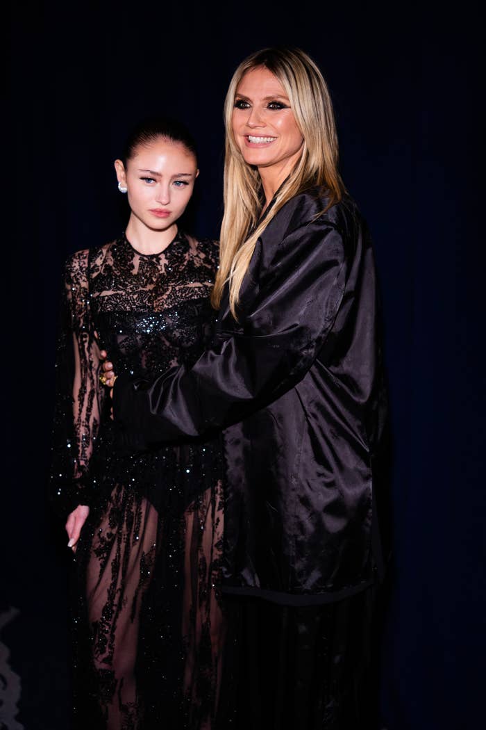 Heidi and Leni Klum pose together; one wears a detailed sheer lace dress, while the other is in a sleek satin coat