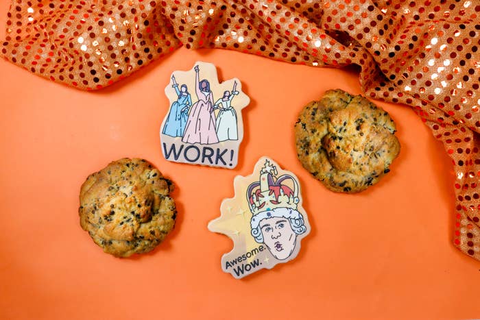 Two cookies and two illustrated cookies; one reads "WORK!" with figures, the other "Awesome. Wow." with a person in a crown. Orange sequin cloth nearby