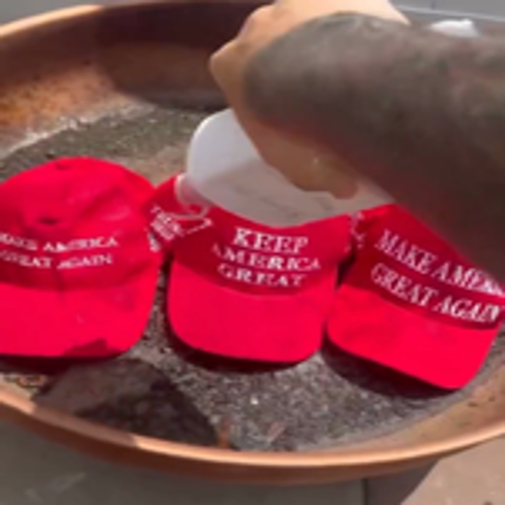 Three red hats with political slogans being soaked with liquid in a pan