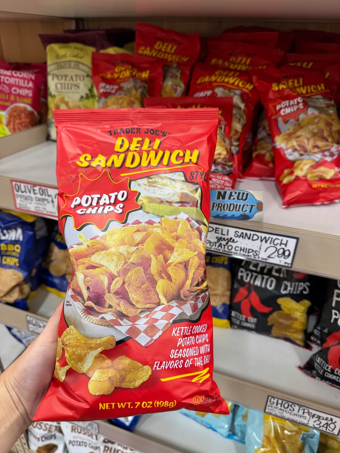 Bag of Trader Joe's Deli Style Potato Chips held in hand, displayed among other chip bags on a store shelf