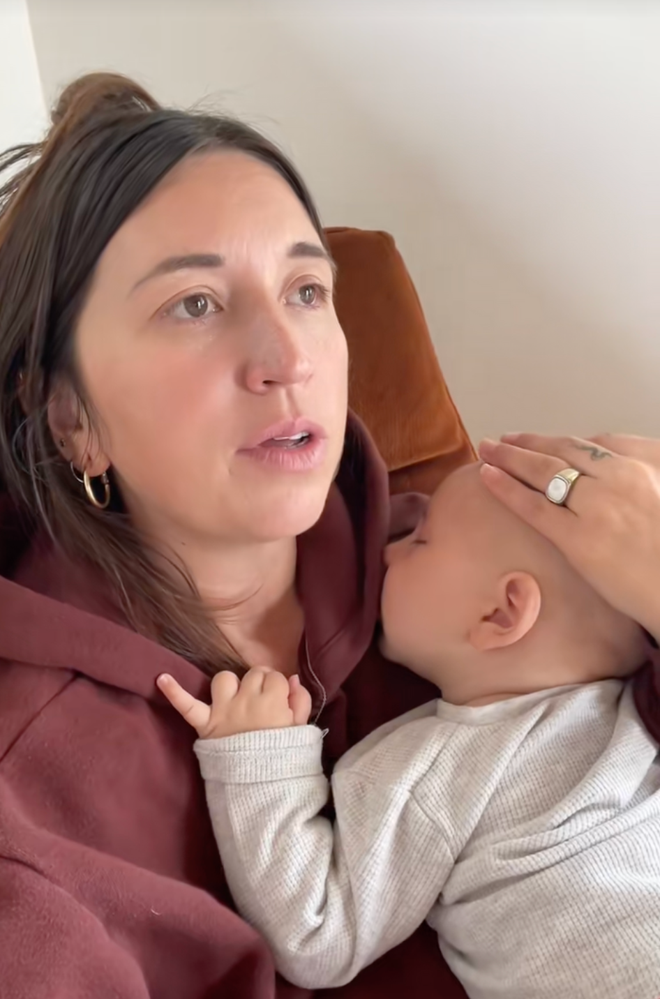 A person holds a sleeping baby close, gently resting a hand on the baby's head