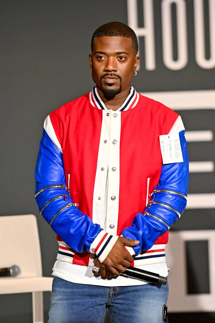 Ray J in letterman-style jacket with blue sleeves and red front holds a microphone on a stage