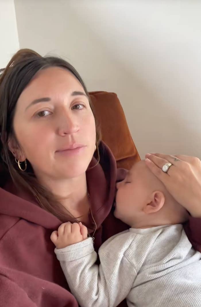 A person is seated, comforting a sleeping baby cradled in their arms while resting against a pillow