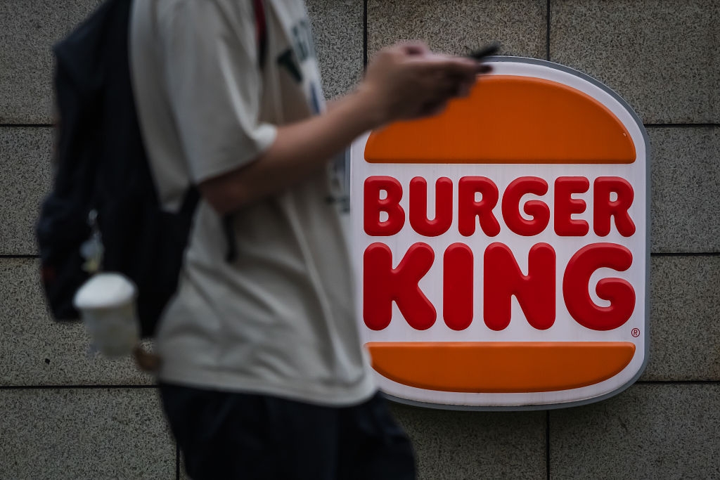Person using phone walks past a Burger King sign attached to a wall