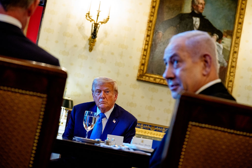 Three men seated at a formal dining table, engaged in conversation, with one man in focus, while two others are slightly blurred