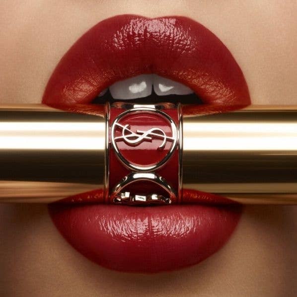 Labios con labial rojo sostienen un tubo dorado de lápiz labial con un logotipo estilizado