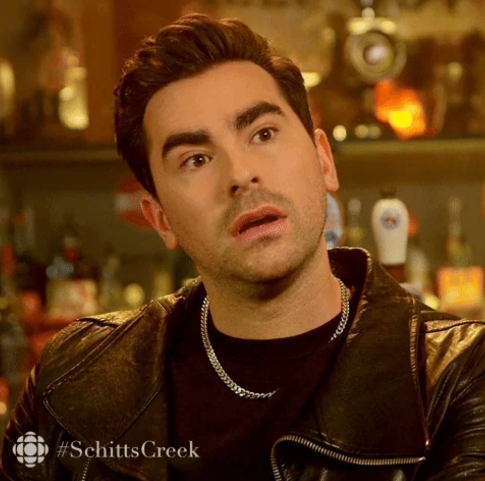 Person med stylet hår i en skinnjakke ser overrasket ut i en barinnstilling. #Schittscreek -logo i hjørnet