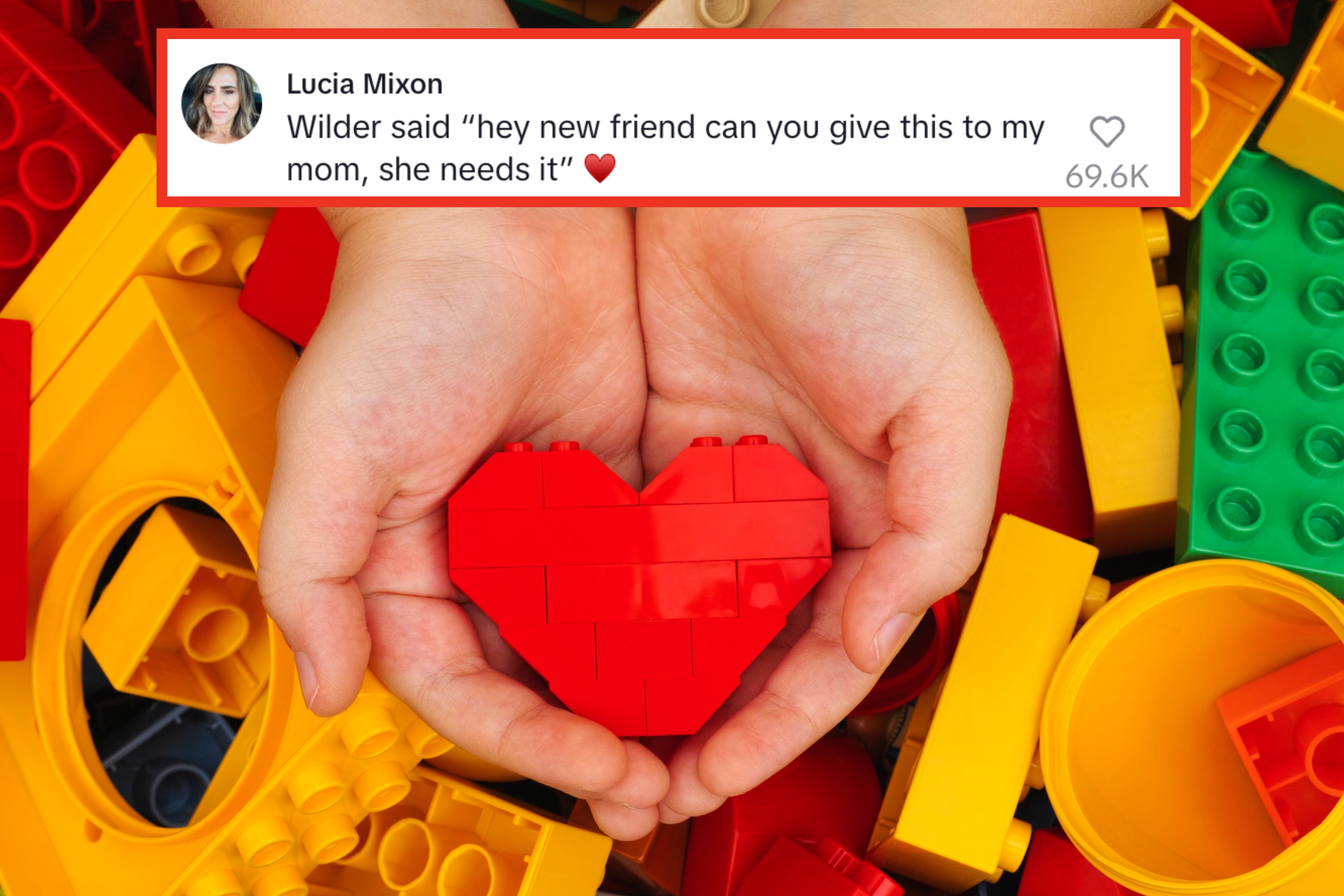 Hands gently holding a red heart-shaped object made from interlocking building blocks, surrounded by scattered colorful blocks