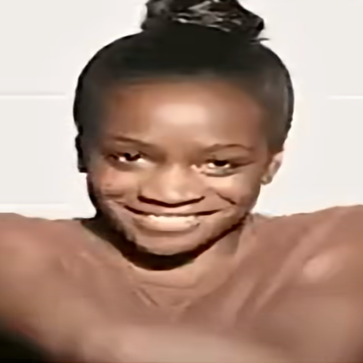 Person smiling with hair in a bun, posing with arms crossed over chest against a simple backdrop