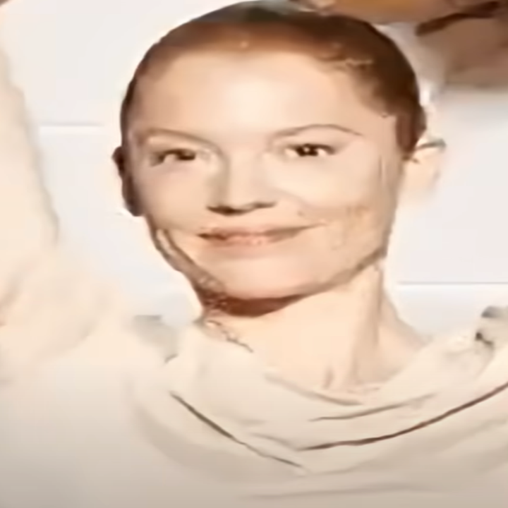 Person smiling with arms raised, wearing a simple top