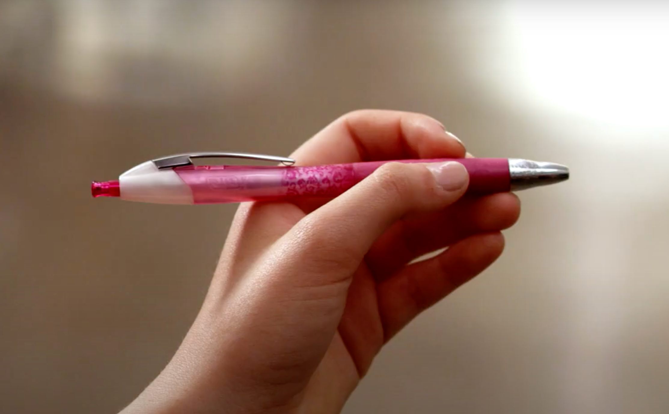 A hand holds a pink retractable pen, poised for use