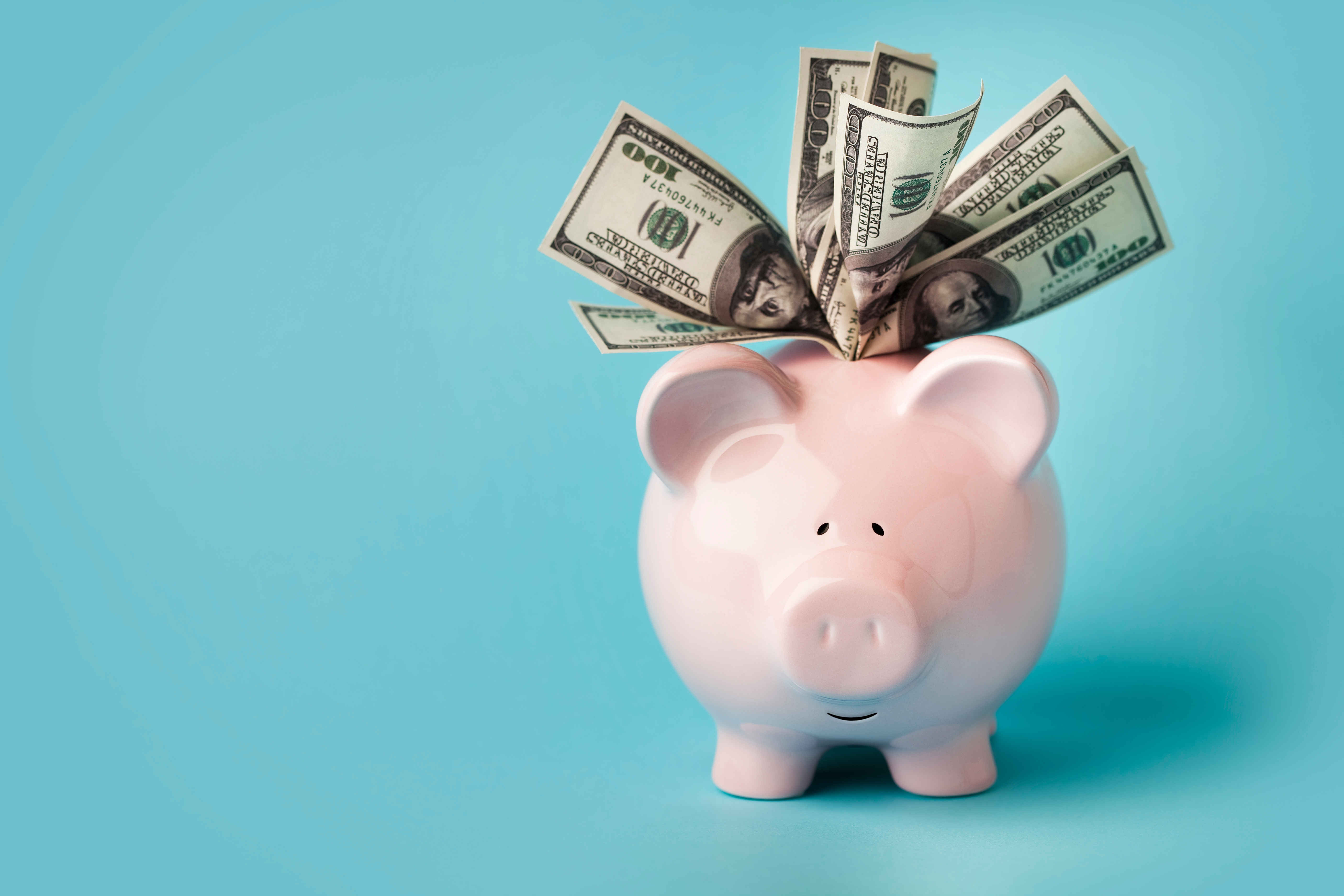 A pink piggy bank overflowing with U.S. dollar bills, symbolizing savings and financial success