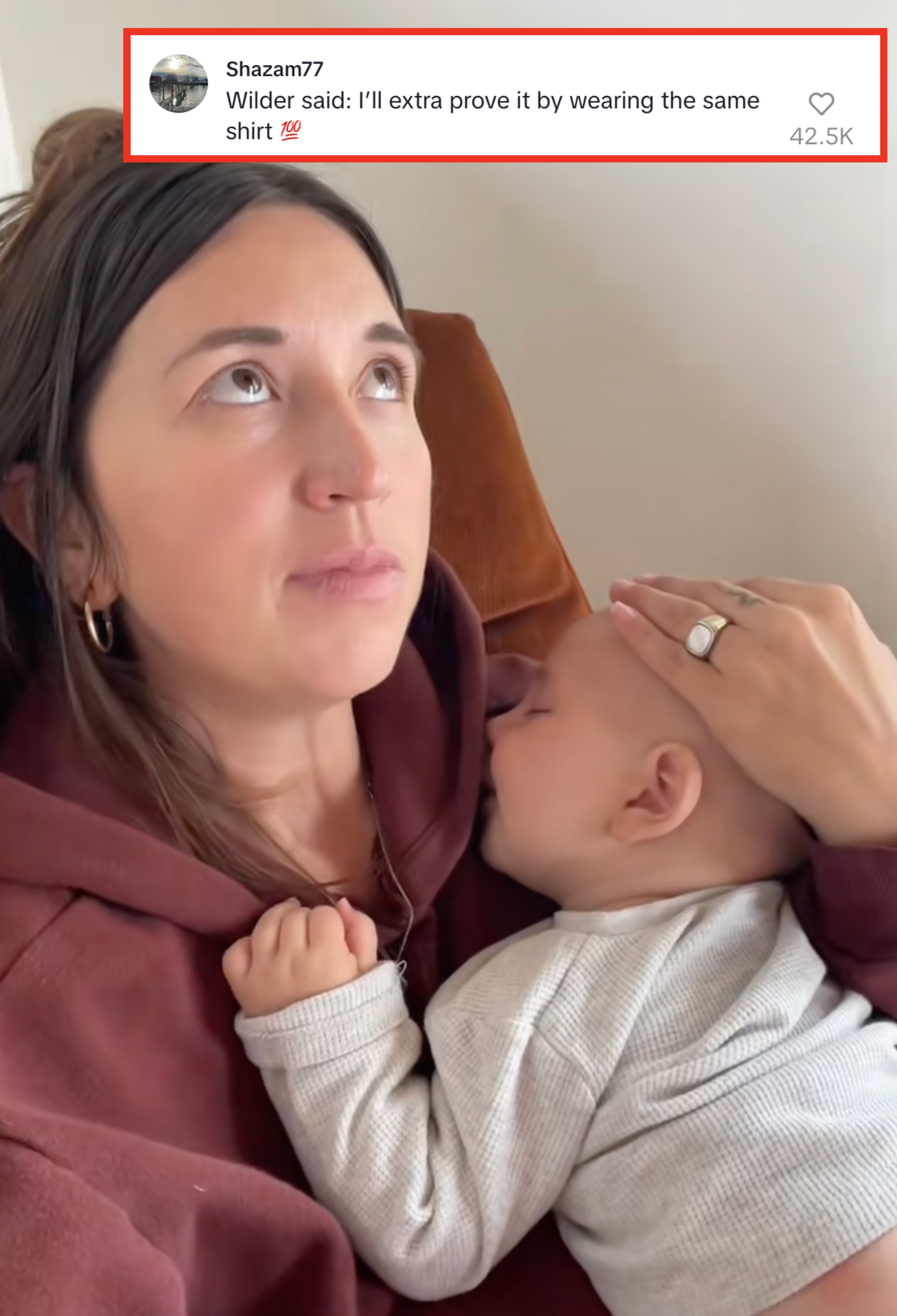 Woman holding a sleeping baby on her chest, looking upwards with a thoughtful expression. Hand gently rests on baby’s head