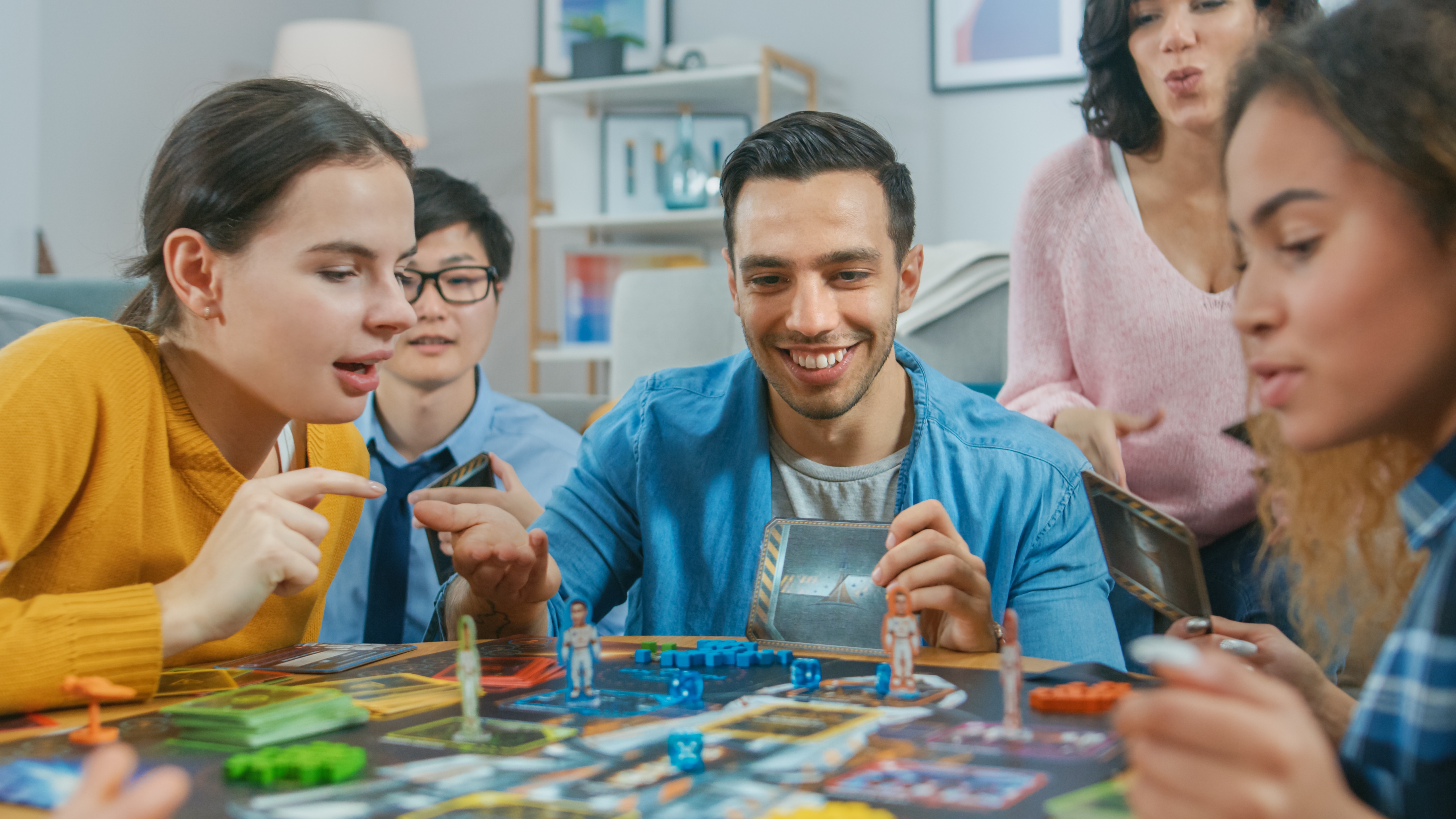 Group of five people playing a board game at a table, focused and engaged in friendly competition