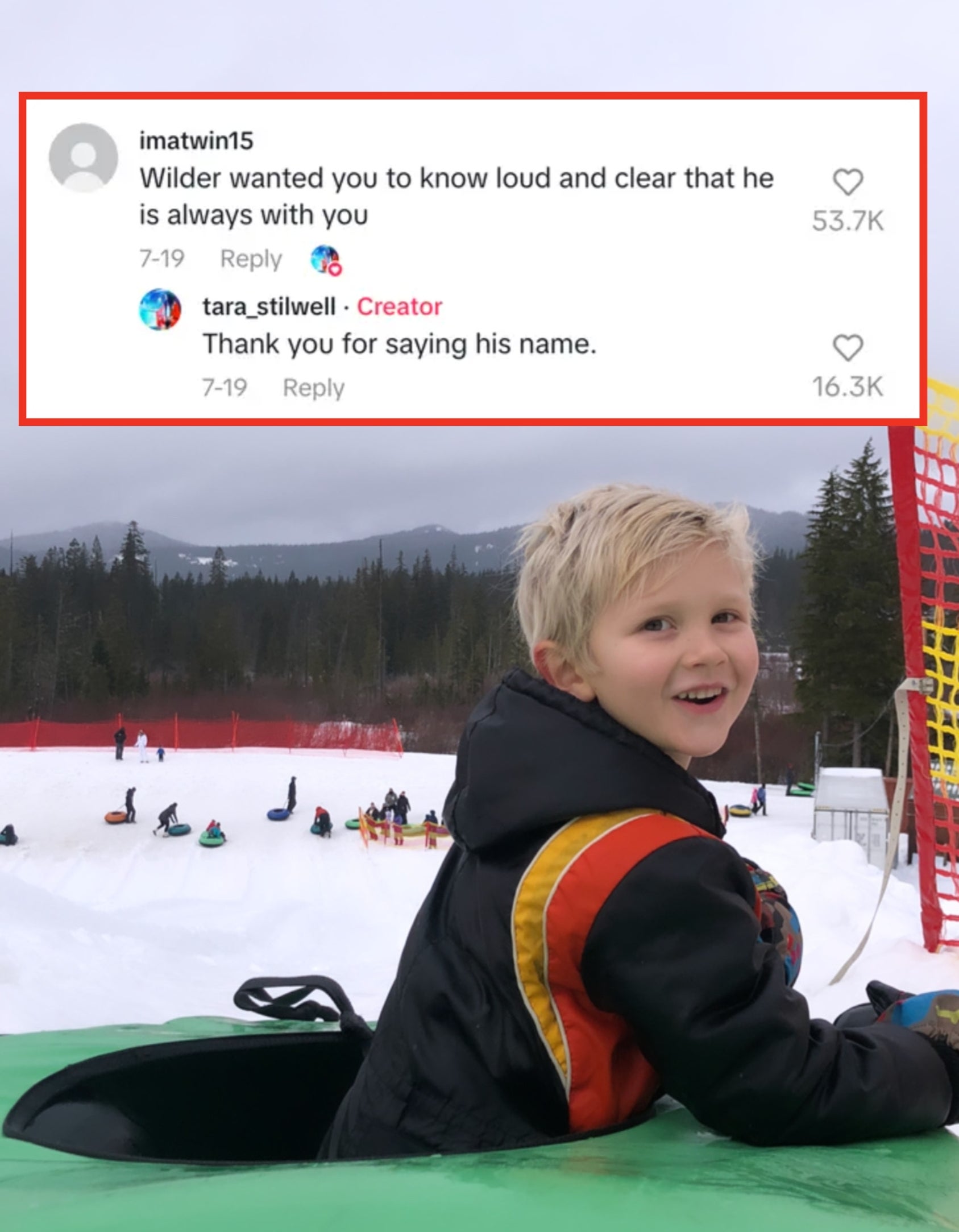Child smiles while in an inner tube at a snowy hill with people tubing in the background