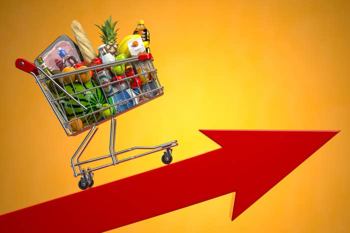 Shopping cart full of groceries balancing on an upward arrow, symbolizing rising costs or inflation