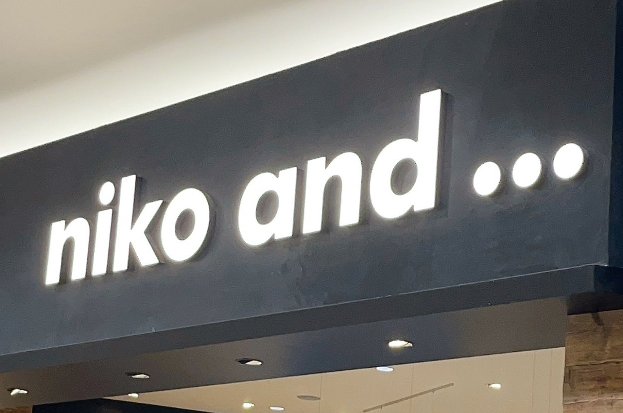 Storefront of "niko and ..." displaying a variety of casual clothing, accessories, and home goods under soft lighting