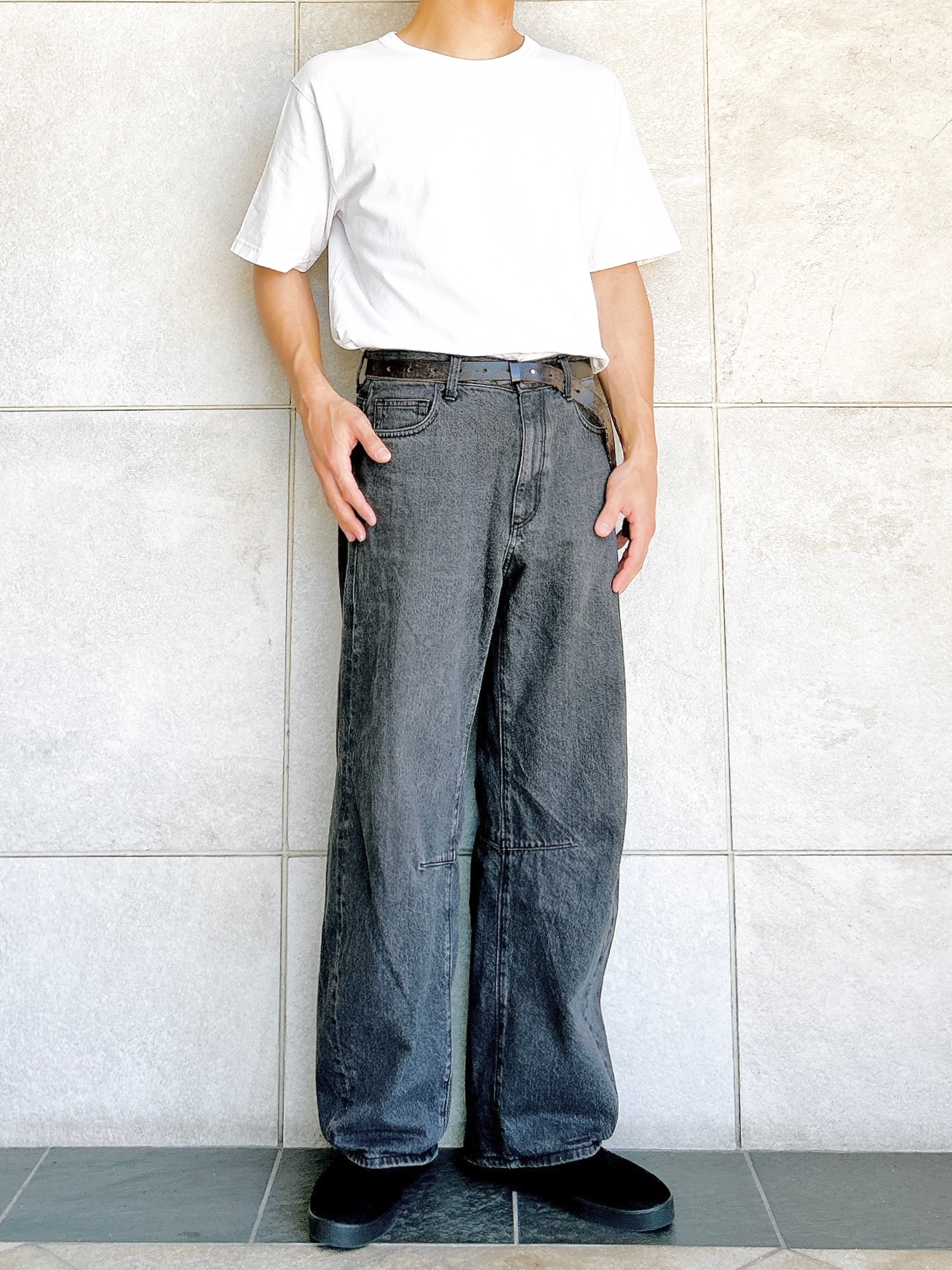 男性がゆったりとしたジーンズとシンプルな白シャツを着用して立っている。