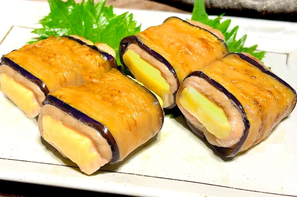 皿に盛られたナスとチーズを薄く巻いた料理。後ろに大葉が添えられている。